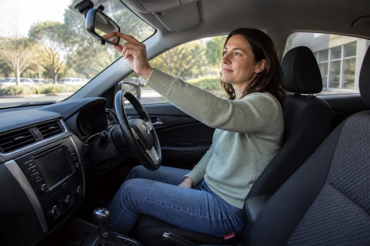 Woman seated in a parked car adjusting the rear-view mirror before driving